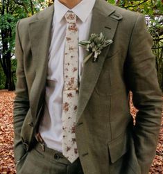 a man wearing a suit and tie standing in leaves