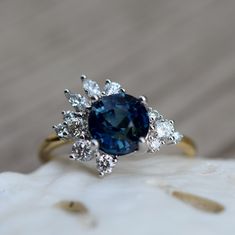 a ring with a blue stone surrounded by white diamonds on top of a piece of wood