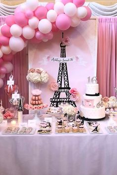 a table topped with lots of pink and white desserts next to a tall eiffel tower