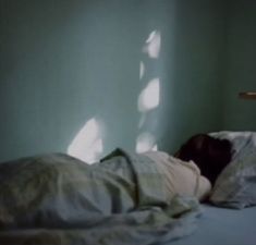 a person is laying in bed with their head on the pillow and shadows cast on the wall behind them