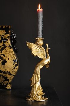 a golden candle holder with a black vase behind it and a gold bird figurine next to it