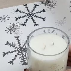 a person holding a lit candle in front of a snowflake wallpaper pattern