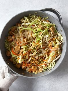 a pan filled with cabbage and carrots on top of a table next to a napkin