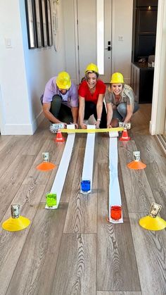 three people in hard hats and yellow helmets are playing with construction blocks on the floor