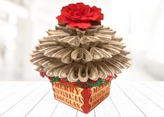 an origami christmas tree made out of dollar bills with a red rose on top