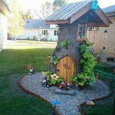 a small tree house built into the side of a tree trunk in a yard with plants growing around it