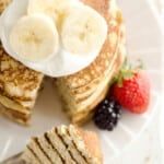 pancakes with banana slices, strawberries and syrup on a white plate topped with sliced bananas