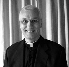 a black and white photo of a man in a priest's outfit smiling at the camera