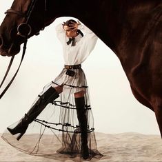 a woman is standing next to a horse wearing boots and a dress with sheer fabric