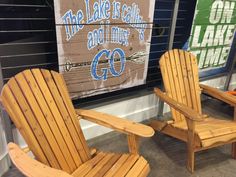 two wooden chairs sitting next to each other in front of a sign that says the lake is calling go