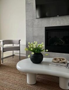 a vase with flowers sitting on a coffee table in front of a tv mounted to the wall