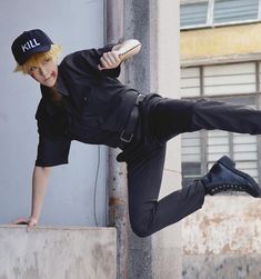 a man in black is leaning on a wall with his leg up and holding a baseball bat