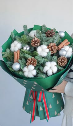 a woman holding a bouquet of pine cones and other christmas decorations in her hand,