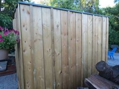 a wooden fence next to a pile of logs and potted plants in the background