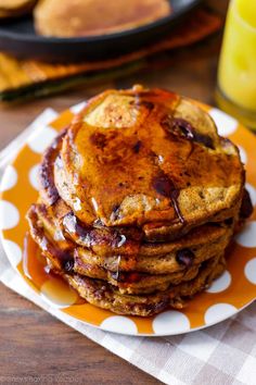 a stack of pancakes sitting on top of a yellow and white plate next to a glass of orange juice