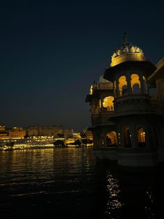 a building sitting on top of a lake next to a tall building with lights on it's sides