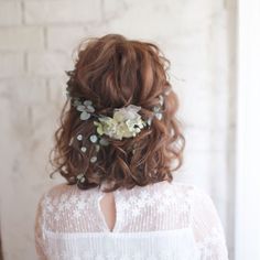 the back of a woman's head with flowers and leaves in her hair, against a white brick wall