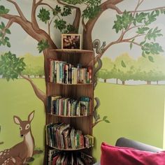 a book shelf with books on it in front of a tree painted on the wall