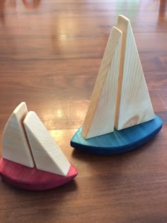 two small wooden sailboats sitting on top of a wooden table next to each other