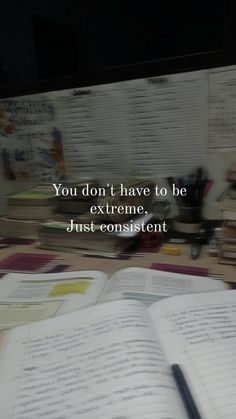 an open book sitting on top of a desk next to a pile of books and a pen