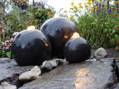 three black balls sitting on top of a rock next to flowers and plants in the background