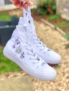 These white monotone Converse trainers are embroidered by hand with my purple floral design.  I offer the option to chose how much embroidery you would like on these particular shoes which vary in price.  - The 'logo embroidery' option is for the leafy design that surrounds the logo on the inside of each shoe.  - The 'outside embroidery' option is for the purple flowers and green foliage which is embroidered on the outside of each shoe.  - The 'all over embroidery' option is for the logo embroidery, outside embroidery, and the date which is embroidered on the back of each shoe if you'd like to make these into bridal or special occasion shoes.  The embroidery is all done in high quality cotton thread to create a completely unique pair of Converse shoes.   I only purchase 100% genuine shoes Purple Embroidered Converse, White Cotton High-top Sneakers With Embroidered Logo, Spring High-top Sneakers With Embroidered Logo, Spring Embroidered High-top Sneakers, White Embroidered Sneakers For Spring, Summer Embroidered High-top Sneakers, White Cotton Sneakers With Floral Embroidery, High-top Sneakers With Embroidered Logo For Spring, High-top Sneakers With Embroidered Graphics For Spring