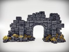 a castle made out of rocks and grass on a white surface with an arch in the middle