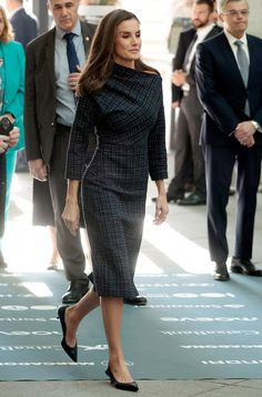 a woman in a black and white dress walking down the street with other people behind her