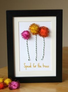 three colorful flowers in a black frame on a table next to some crochet beads