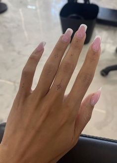 a woman's hand with pink and white nail polish on her nails, sitting in front of a black chair