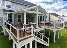 a deck with chairs and an umbrella in the grass near a house on a sunny day