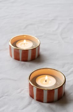 two orange and white striped candle holders sitting on top of a bed next to each other