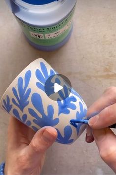 someone is painting a vase with blue flowers on the outside and white designs on the inside