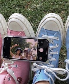 three pairs of shoes are sitting in the grass and one is holding a cell phone