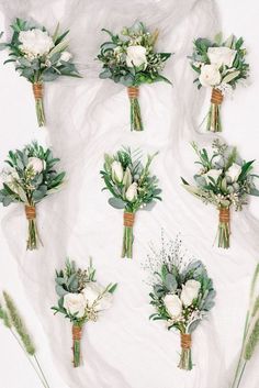 wedding bouquets laid out on a white sheet with greenery and flowers in them