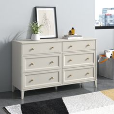 a white dresser sitting in a room next to a window with a potted plant on top of it