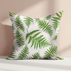 a white pillow with green leaves on it sitting on a shelf next to a pink wall