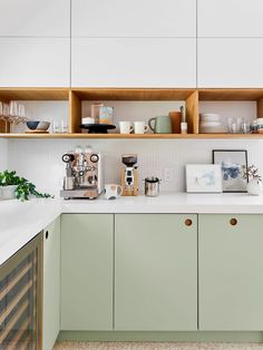 a kitchen with green cupboards and white counter tops, filled with coffee pots and cups