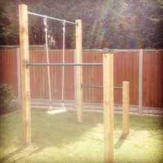 a wooden swing set with swings and bars in the back yard, next to a fence