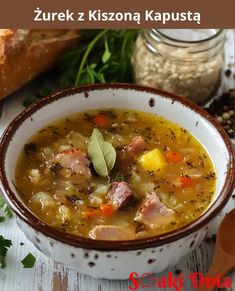 there is a bowl of soup with meat and vegetables in it on the table next to bread