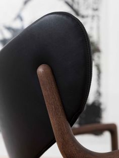 the back of a black leather chair with wooden legs and arm rests on a wood table