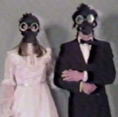 two people wearing gas masks standing next to each other in formal clothing and tuxedos