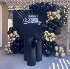 a happy birthday sign surrounded by black and gold balloons