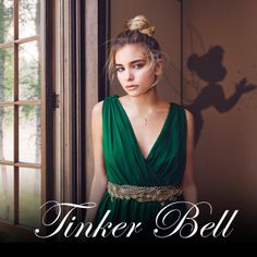 a woman in a green dress standing next to a window with the words tinker bell on it