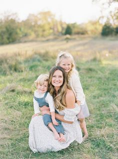 a mother and her two children are sitting in the grass with their arms around each other