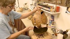 a woman is working on a clay mask in her studio with lots of crafting supplies