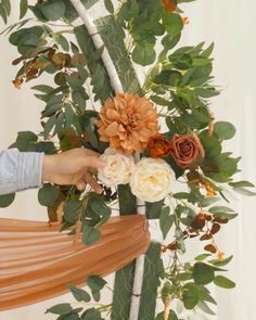 a woman is arranging flowers in a vase on a table with greenery around her