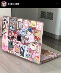 an open laptop computer sitting on top of a wooden table covered in stickers and decals