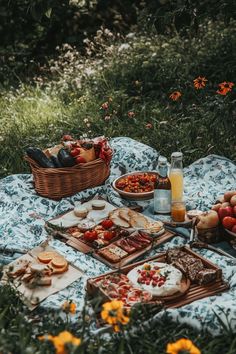 an outdoor picnic with food and drinks on the blanket in front of it, surrounded by wildflowers