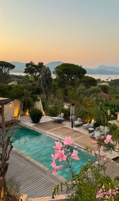 an outdoor swimming pool surrounded by greenery and trees at sunset with the ocean in the background